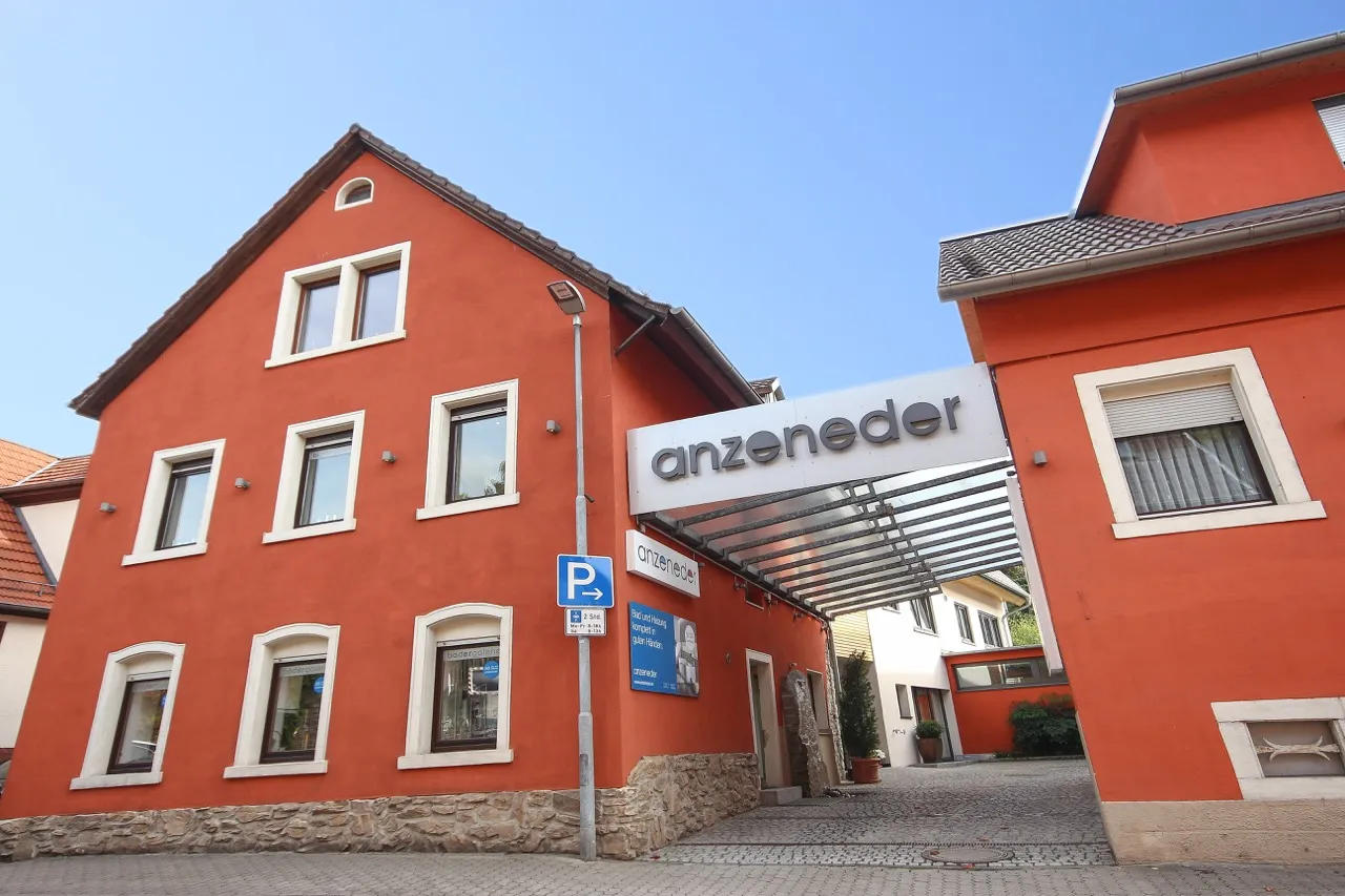 Außenansicht des Firmengebäudes von Anzeneder mit rot verputzter Fassade, überdachtem Eingangsbereich und Firmenlogo an der Straßenfront.