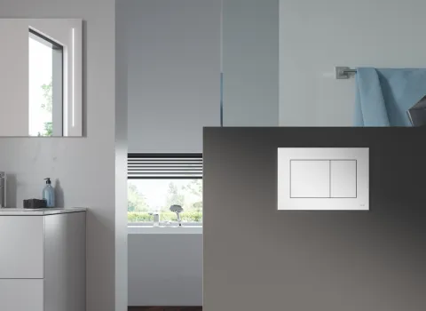 Blick in ein minimalistisches Badezimmer mit einer weißen TECEnow-WC-Betätigungsplatte, die zentral auf einer dunkelgrauen Wand montiert ist.