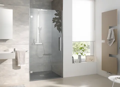 Helles Bad mit in Nische eingebauter Glasdusche HSK Atelier Plan, beige-grauen Fliesen, schlichtem Waschtisch und stilvollem Handtuchheizkörper vor einem großen Fenster.