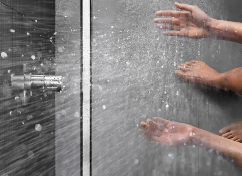 Ein Wasserstrahl trifft auf eine Person, deren Hände und Füße unter der Dusche zu sehen sind.