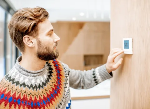 In einem modernen Wohnraum mit Holzoptik bedient ein Mann einen Thermostat zur Steuerung der Klimaanlage.