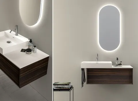 Doppelansicht eines eleganten Badezimmers von Stocco mit dunkel gemasertem Unterschrank, weißer Waschtischplatte und beleuchtetem Ovalspiegel.