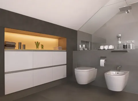 Minimalistisches Badezimmer mit grauen Wandflächen, wandhängendem WC, Bidet und beleuchteter Nische mit Badaccessoires.