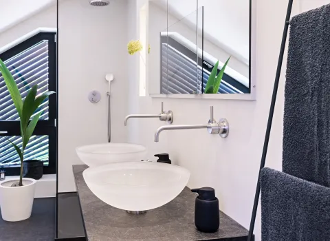 Modernes Dachbad mit Doppelwaschtisch, schwarzen Natursteinplatten und bodengleicher Glasdusche.