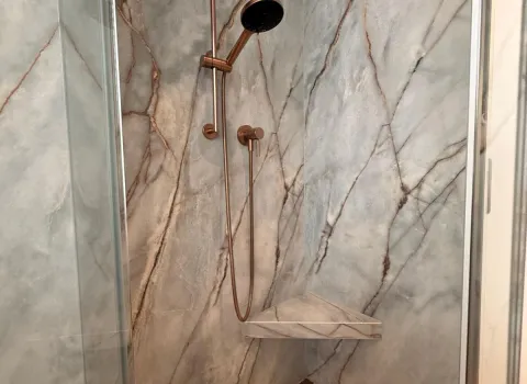 Detailaufnahme einer modernen Walk-in-Dusche mit eleganter Armatur in Kupferoptik und marmorierter Wandgestaltung.