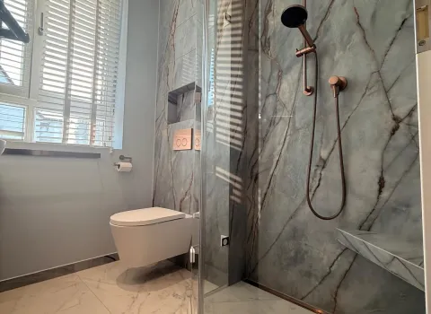 Helles Badezimmer mit bodengleicher Dusche, wandhängendem WC und stilvoller Wandverkleidung in Marmoroptik.