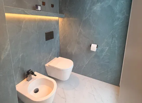 Elegantes Gästebad mit großformatiger Natursteinoptik, wandhängendem WC und indirekter LED-Beleuchtung in warmem Ambiente.