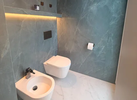 Elegantes Gästebad mit großformatiger Natursteinoptik, wandhängendem WC und indirekter LED-Beleuchtung in warmem Ambiente.