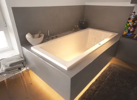 Graue Whirlpool-Badewanne mit warmer Unterbodenbeleuchtung, Handtüchern und modernen Armaturen in stilvollem Badezimmer.