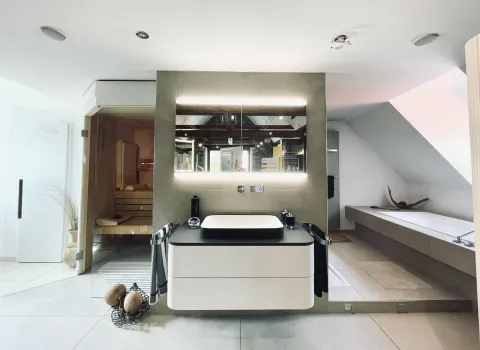 Großzügiges Wellnessbad mit Sauna, beleuchtetem Spiegel und freistehendem Waschtisch.