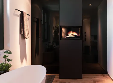 Freistehende Badewanne vor dunkler Wandgestaltung mit integriertem Kamin für eine wohnliche Atmosphäre.