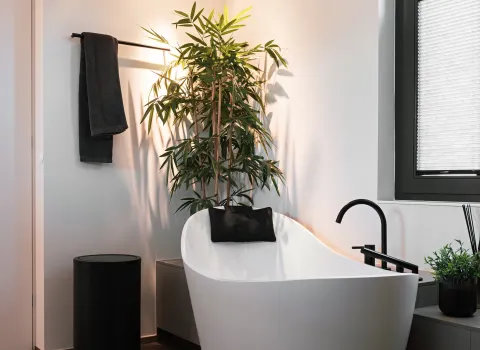 reistehende weiße Badewanne mit schwarzer Armatur vor großem Fenster in modernem Bad.