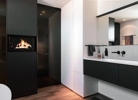 Exklusives Badezimmer mit dunklem Waschtisch, großem Spiegel und integriertem Kamin als Blickfang.