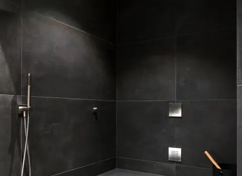 Moderne Dampfdusche mit integrierter Sitzbank, dunklen Fliesen und stilvollem Sauna-Zubehör.