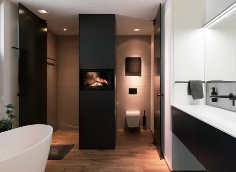 Modernes Badezimmer mit zentraler Trennwand, integriertem Kamin und separatem WC-Bereich im Hintergrund.