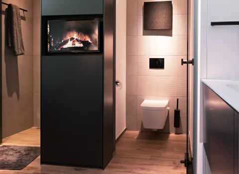 Modernes Badezimmer mit zentraler Kamin-Trennwand und Blick auf den abgetrennten WC-Bereich.