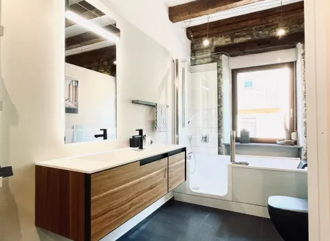 Stilvolles Badezimmer mit Holzwaschtisch, schwarzen Armaturen und sichtbaren Deckenbalken.