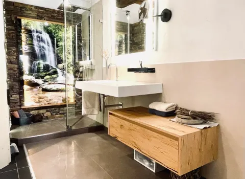 Modernes Badezimmer mit Holzwaschtisch, Glasdusche und großflächigem Wasserfallmotiv als Blickfang.
