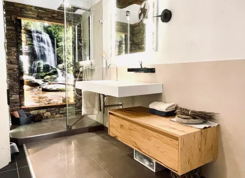 Modernes Badezimmer mit Holzwaschtisch, Glasdusche und großflächigem Wasserfallmotiv als Blickfang.