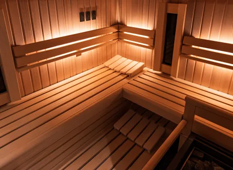 Eckbereich einer modernen Sauna mit mehrstufigen Holzbänken und warmem indirektem Licht.