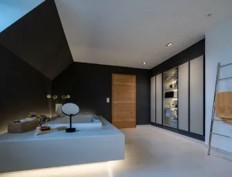 Großzügiges Badezimmer mit eingelassener Badewanne, dunklen Wänden, Einbauschränken und modernem Lichtkonzept.