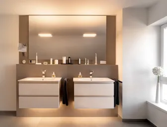 Modernes Badezimmer mit zwei schwebenden Waschtischen, großem Spiegel und indirekter Beleuchtung in warmen Naturtönen.