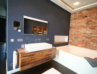 Stilvolles Badezimmer mit Holzwaschtisch, freistehender Badewanne und Backsteinwand in dunklem Ambiente.