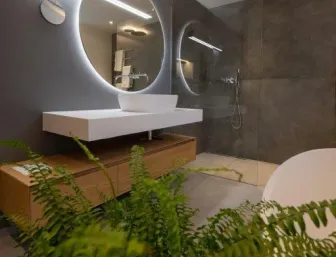 Stilvoller Waschplatz mit beleuchtetem Rundspiegel, Aufsatzwaschbecken und bodengleicher Dusche in modernem Badezimmer.
