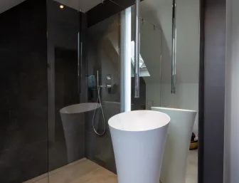 Elegantes Badezimmer mit freistehendem Waschbecken, raumhohem Spiegel und bodengleicher Regendusche in dunklem Fliesendesign.