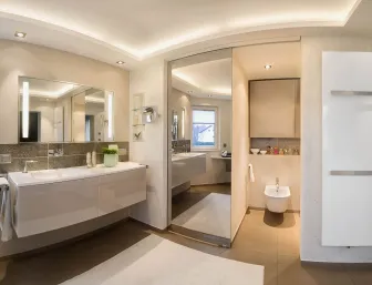 Elegantes Badezimmer mit großem Waschtisch, beleuchtetem Spiegel, separatem Bidetbereich und hochwertiger Lichtgestaltung.