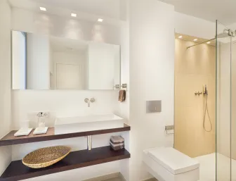 Helles Badezimmer mit wandhängendem Waschtisch, großem Spiegel, WC und bodengleicher Dusche mit Glasabtrennung.