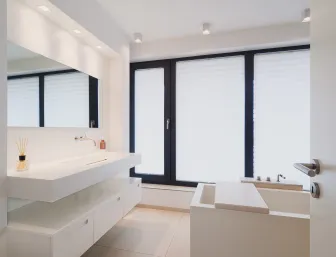 Minimalistisches Badezimmer mit freistehender Badewanne, großem Waschtisch, wandfüllendem Spiegel und bodentiefen Fenstern.