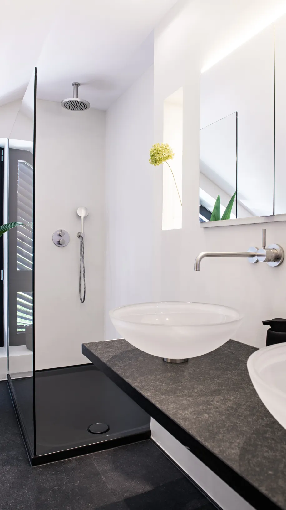 Minimalistisches Dachbad mit zwei Aufsatzwaschbecken, dunkler Natursteinplatte und offener Glasdusche.