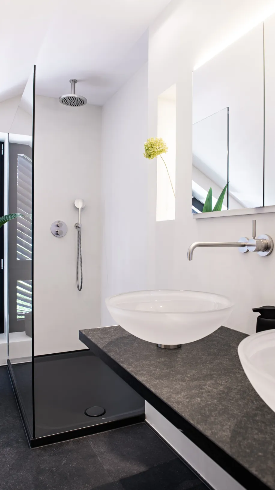 Minimalistisches Dachbad mit zwei Aufsatzwaschbecken, dunkler Natursteinplatte und offener Glasdusche.