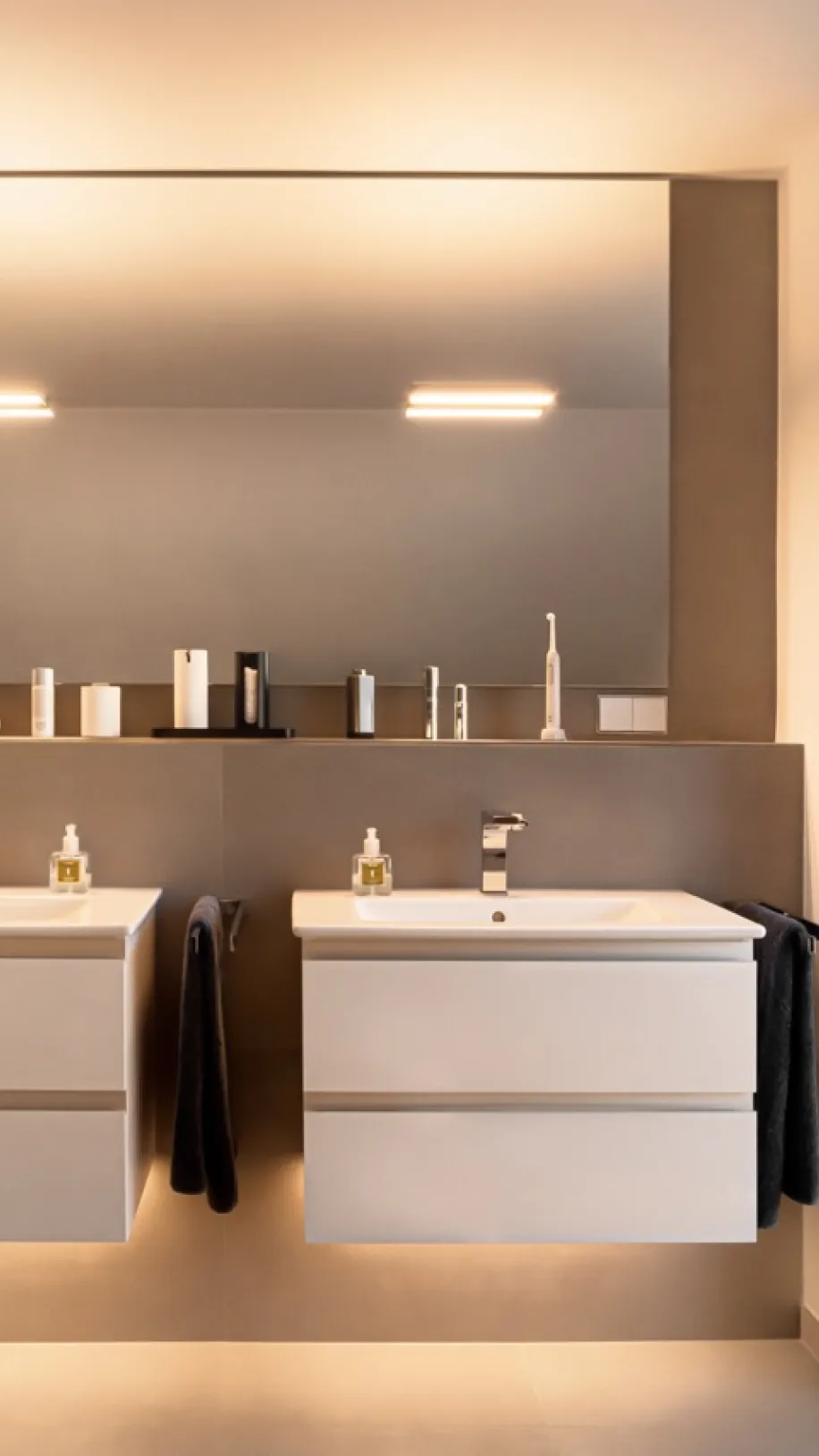 Modernes Badezimmer mit zwei schwebenden Waschtischen, großem Spiegel und indirekter Beleuchtung in warmen Naturtönen.