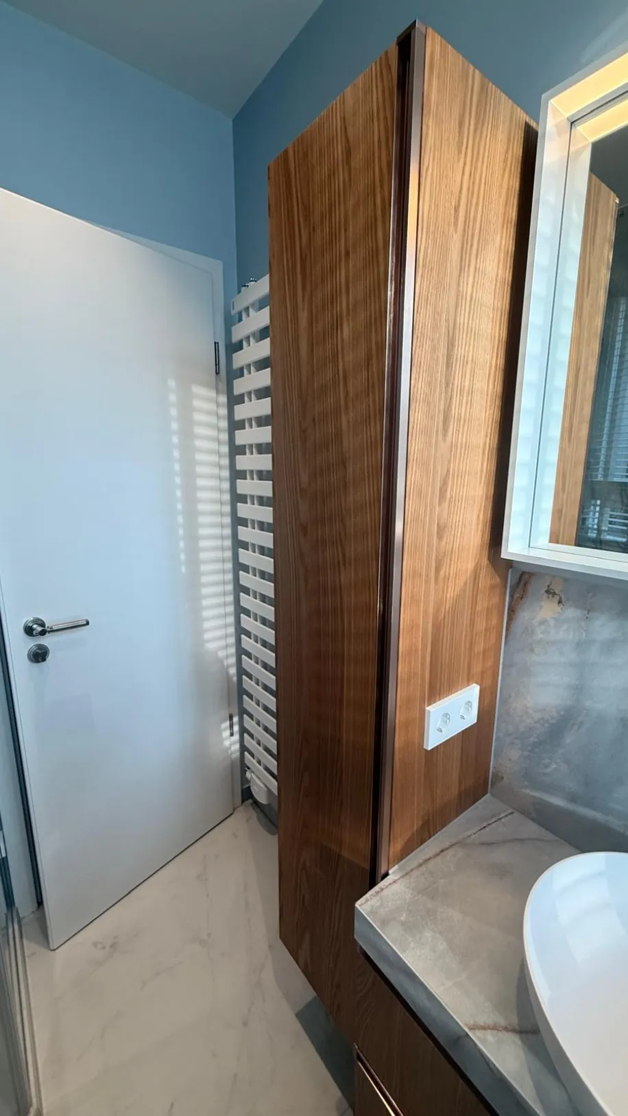 Modernes Badezimmer mit maßgefertigtem Holzhochschrank, Aufsatzwaschbecken und großformatigen Fliesen in Marmoroptik.