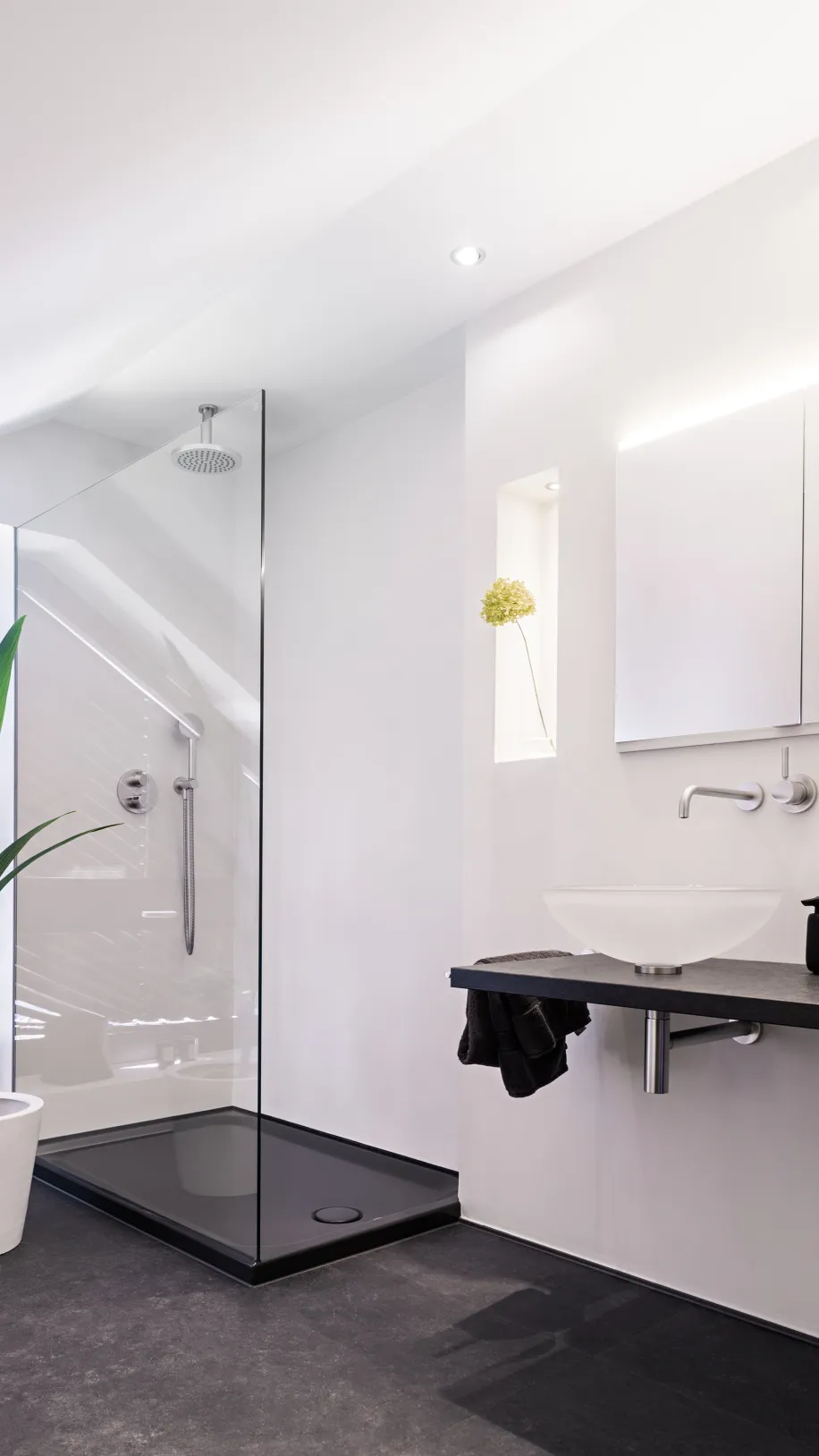 Helles Badezimmer mit freistehendem Waschbecken, schwarzer Waschtischplatte und bodengleicher Glasdusche.