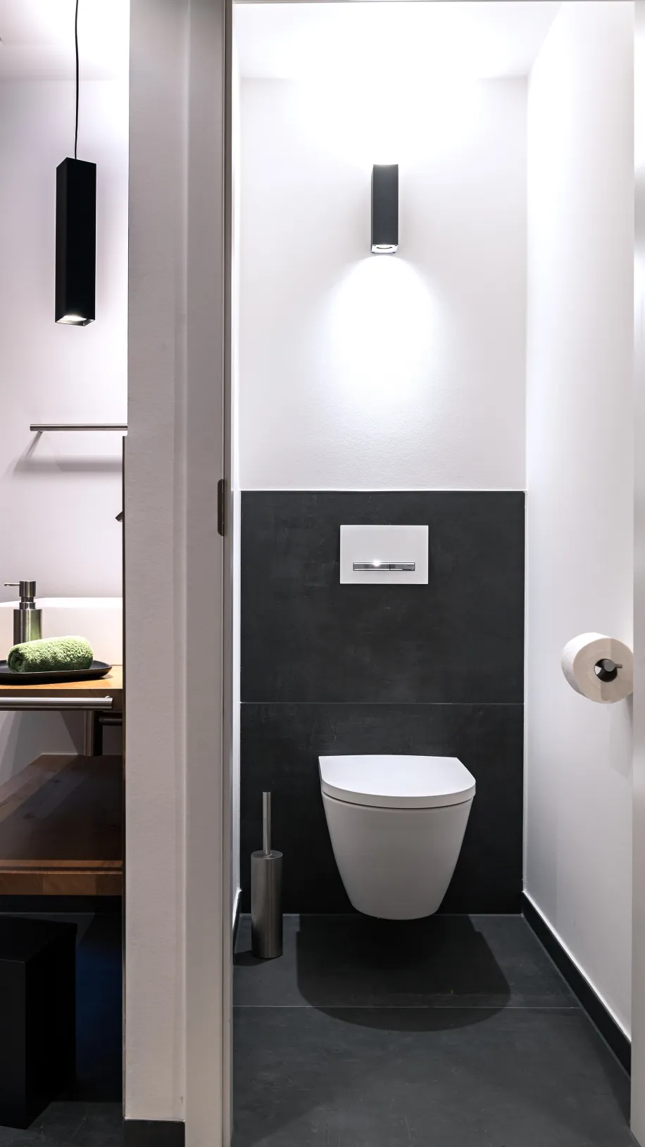 Separates Gäste-WC mit wandhängender Toilette, dunklen Fliesen und minimalistischer Beleuchtung.