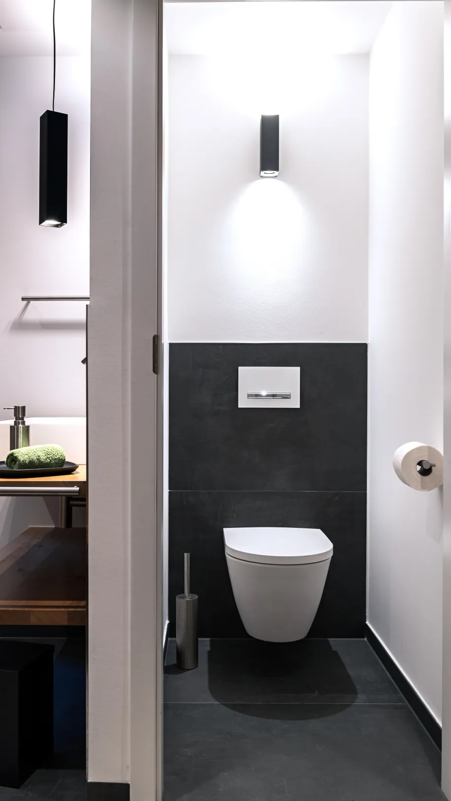 Separates Gäste-WC mit wandhängender Toilette, dunklen Fliesen und minimalistischer Beleuchtung.