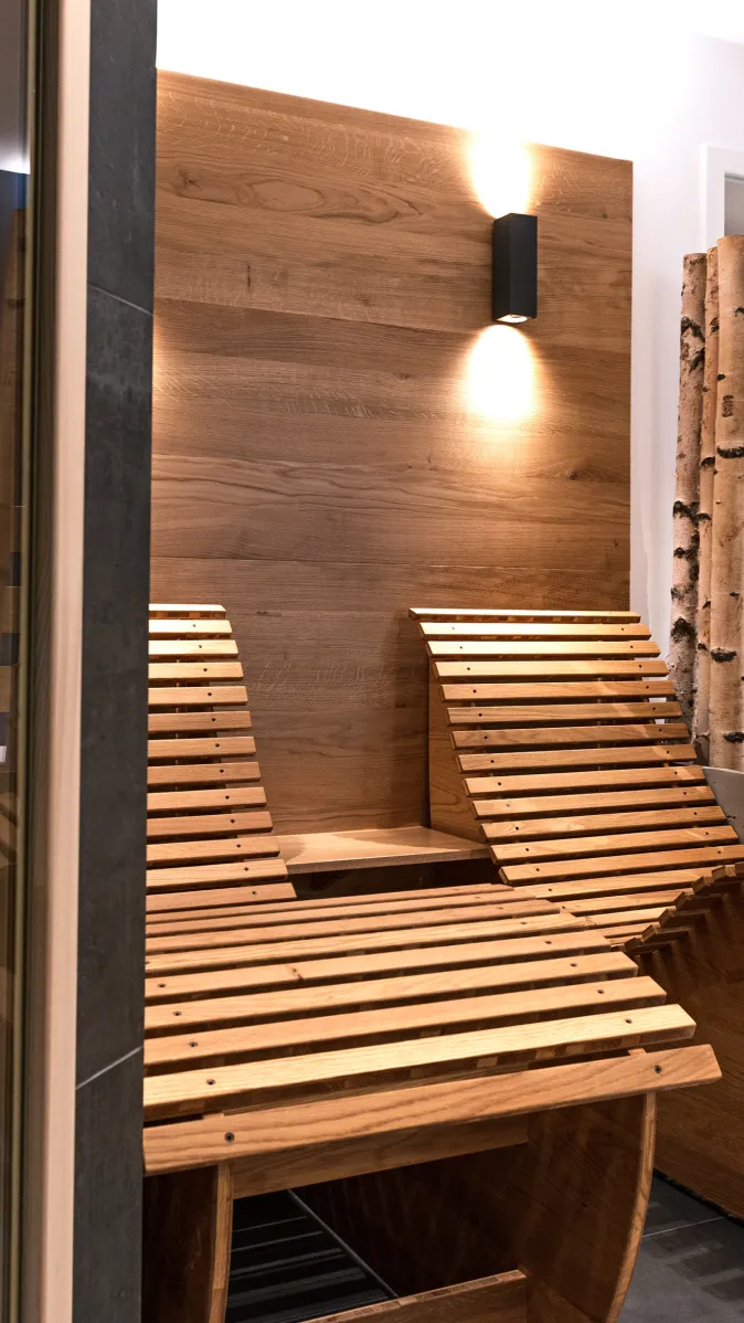 Wellnessbereich mit zwei geschwungenen Holzliegen, Holzwandverkleidung und dekorativer Birkenstamm-Abtrennung.