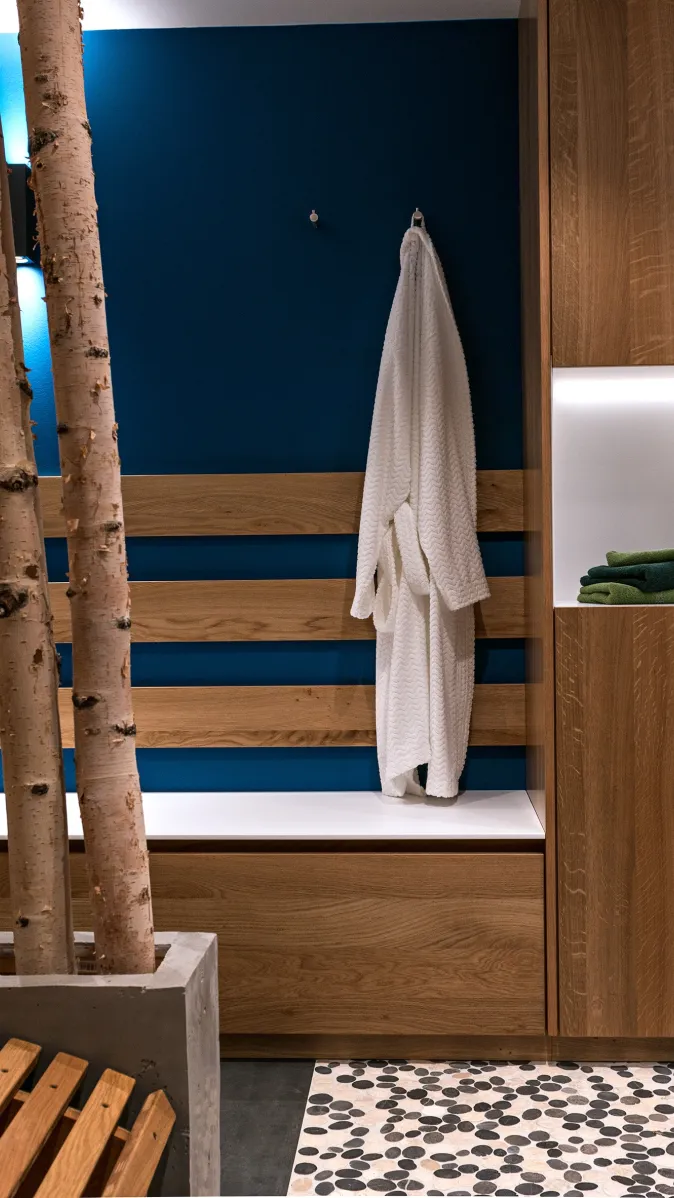 Umkleide- und Wellnessbereich mit Holzschränken, beleuchteten Regalfächern, Sitzbank und aufgehängtem weißen Bademantel.