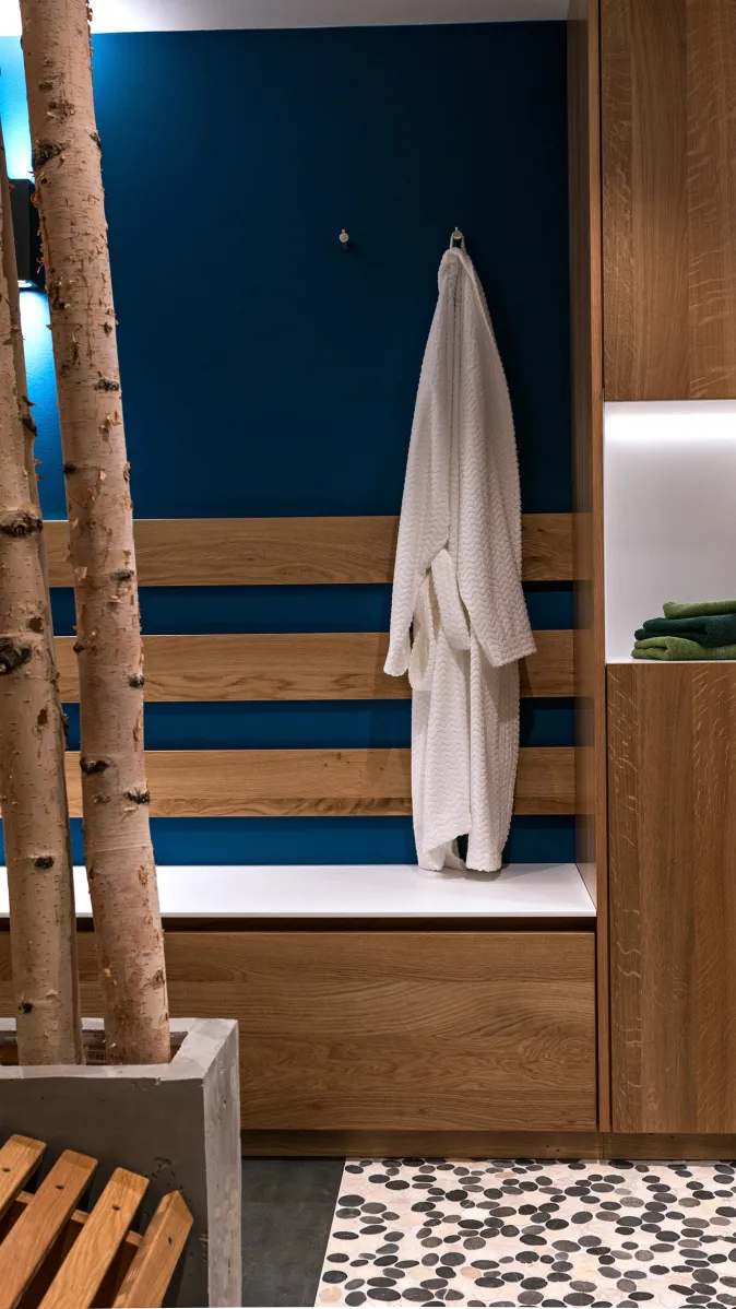 Umkleide- und Wellnessbereich mit Holzschränken, beleuchteten Regalfächern, Sitzbank und aufgehängtem weißen Bademantel.