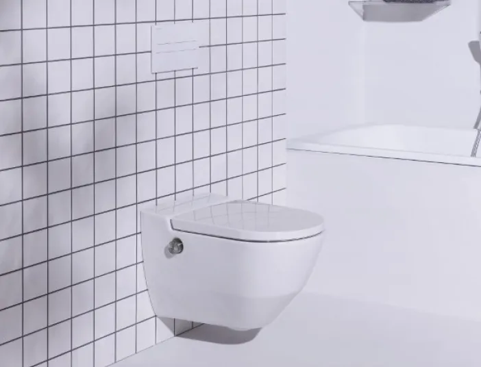 Ein modernes Badezimmer mit einer schwebenden weißen Toilette, die an einer gefliesten Wand mit quadratischen Kacheln montiert ist.